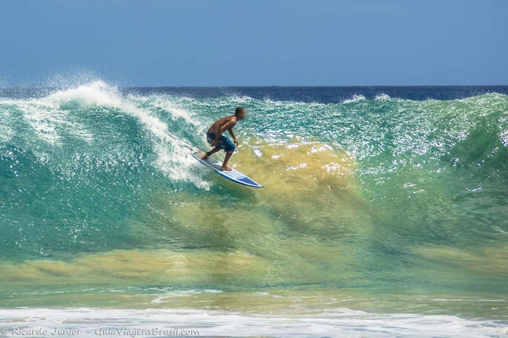 Imagem de surfista nas águas multicoloridas de Noronha.